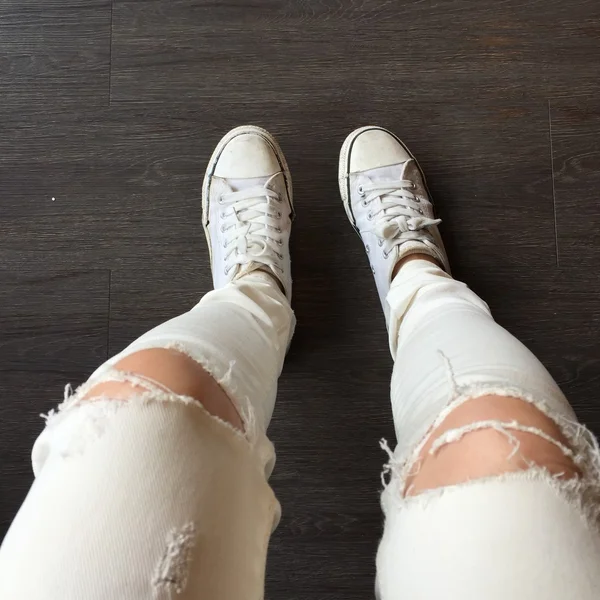 年轻时尚女性的腿部穿着牛仔裤和运动鞋在地板上 — 图库照片