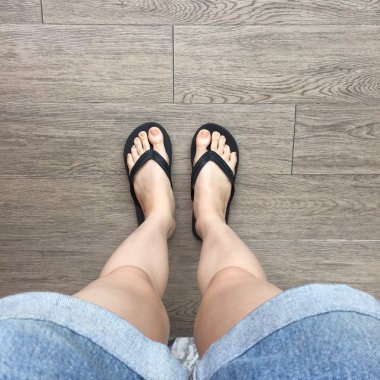 Genç kız bacaklarını ahşap zemin üzerinde siyah Flipflop Sandaletler içinde