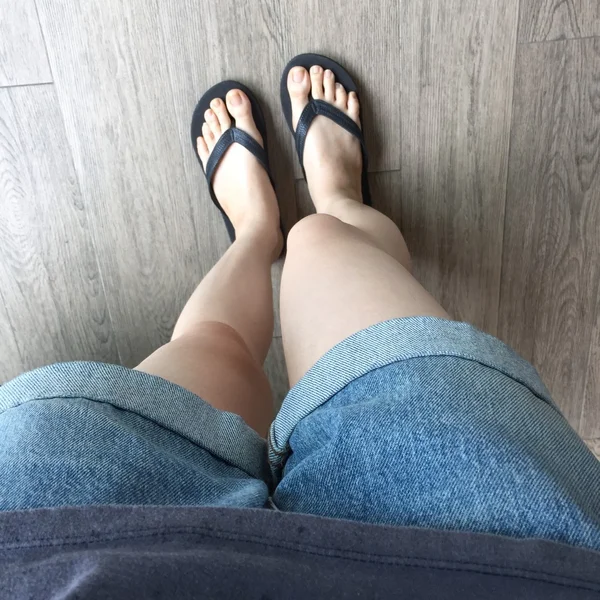 Jong meisje benen in zwarte Flipflop sandalen op houten vloer — Stockfoto