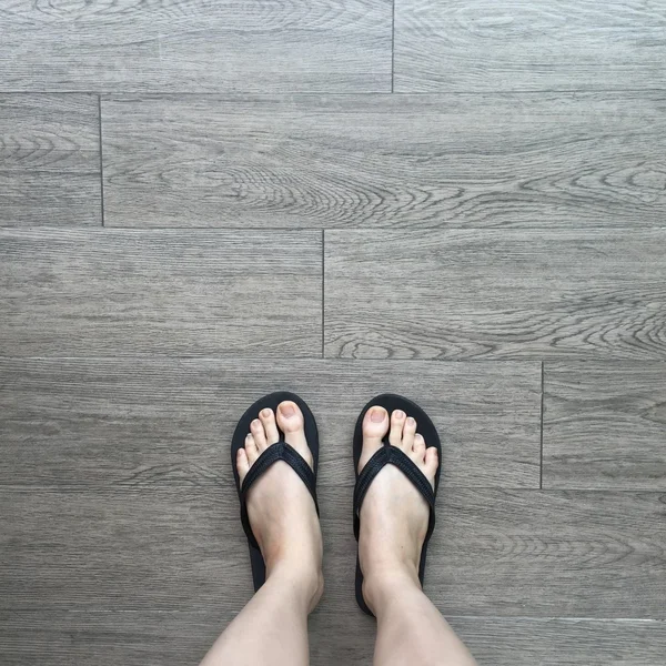 Piernas de niña en sandalias Flipflop Negro en piso de madera —  Fotos de Stock