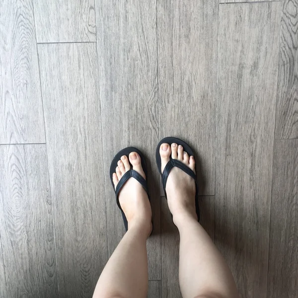 Piernas de niña en sandalias Flipflop Negro en piso de madera — Foto de Stock