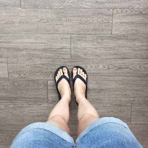 Jong meisje benen in zwarte Flipflop sandalen op houten vloer — Stockfoto
