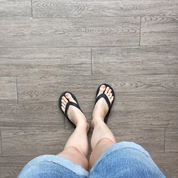 Giovane ragazza gambe in nero Flipflop sandali sul pavimento in legno — Foto Stock