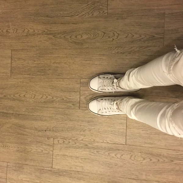 Λευκά αθλητικά παπούτσια στα πόδια κορίτσι σε φόντο ξύλινη — Φωτογραφία Αρχείου
