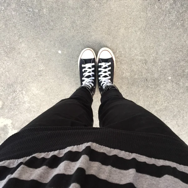 Schwarze Turnschuhe an Mädchenbeinen. Frau in schwarzen Jeans und Turnschuhen — Stockfoto