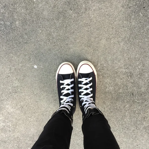Zapatillas negras en piernas de chica. Mujer en jeans negros y zapatillas deportivas —  Fotos de Stock
