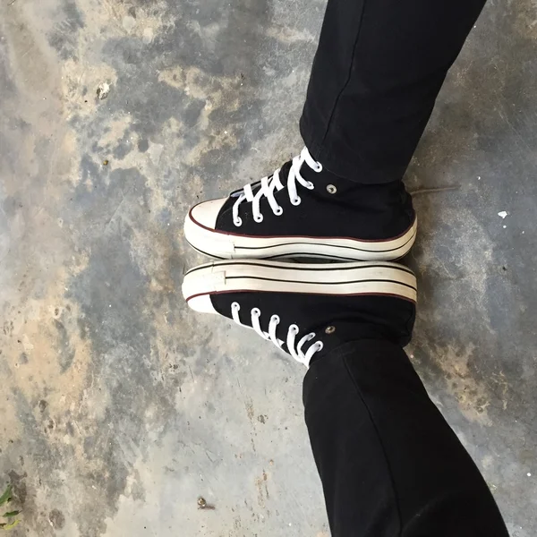 Zapatillas negras en piernas de chica. Mujer en jeans negros y zapatillas deportivas —  Fotos de Stock