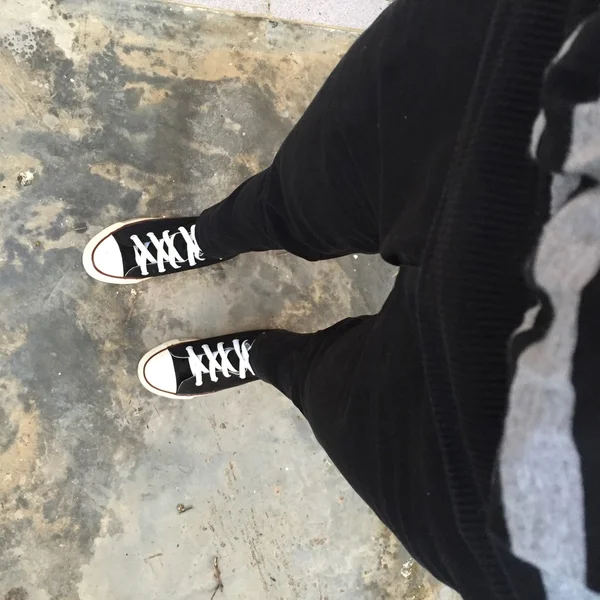 Sapatilhas pretas em pernas de menina. Mulher de calça preta e tênis — Fotografia de Stock