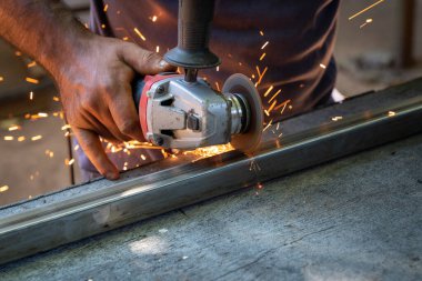 Kıvılcım saçan dairesel elektrikli bir aletle metal çubuk kesen bir adam.