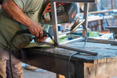 Metalurji atölyesinde metal sandalyeye kaynak yapan bir adam.