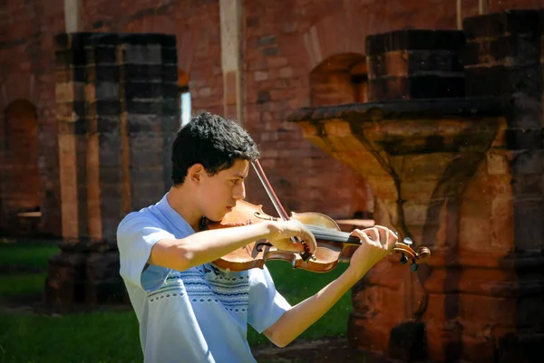 Genç bir kemancı, gün ortası güneşinin altında kızıl taş yıkıntılarının önünde gösteri yapıyor. Kemanin sicak tonlari tarihi ortamla harmanlanmis, sanat ve miras arasinda zamansiz bir uyumu hatirlatiyor..