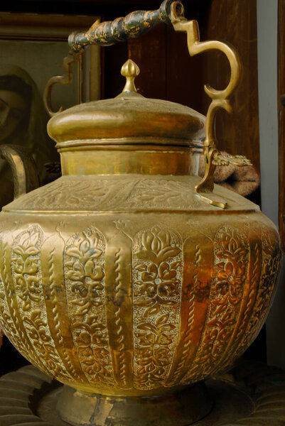 Крупный план старинного медного сосуда с детальной цветочной гравировкой и декоративной ручкой, отражающей традиционное металлическое мастерство и историческую элегантность.