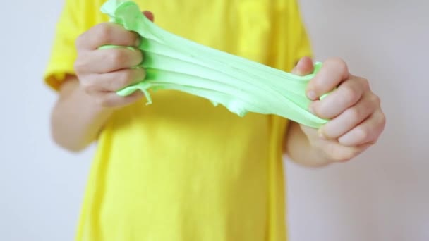 녹색 점액을 가까이 대고 손을 잡으세요. 노란 티셔츠를 입은 아이가 미끄럼을 타고 있습니다. 손에 쥐고 있는 유행성 액체 장난감. 손을 흔들며 놀고 있는 아이들. — 비디오