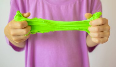 Yeşil sümüklü eller, yaklaşın. Mor tişörtlü, balçık geren bir çocuk. Modaya uygun sıvı oyuncak ellere yapışıyor. Çocuk elleri sümük oyuncağı oynuyor.