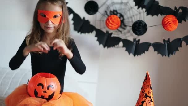 Маленькая девочка в костюме ведьмы с конфетным ведром тыквы Хэллоуин дома, колдует и творить магию. Хаус пати Хэллоуин. Праздничный декор — стоковое видео