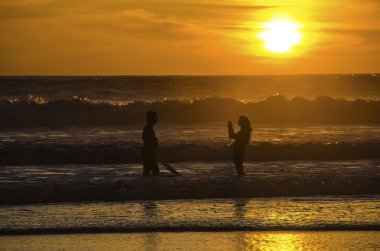 sörfçü dalgaları günbatımında Portekiz'de izliyor..