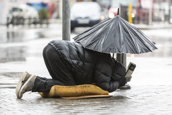 Mendicante senzatetto con ombrello sotto la pioggia — Foto Stock