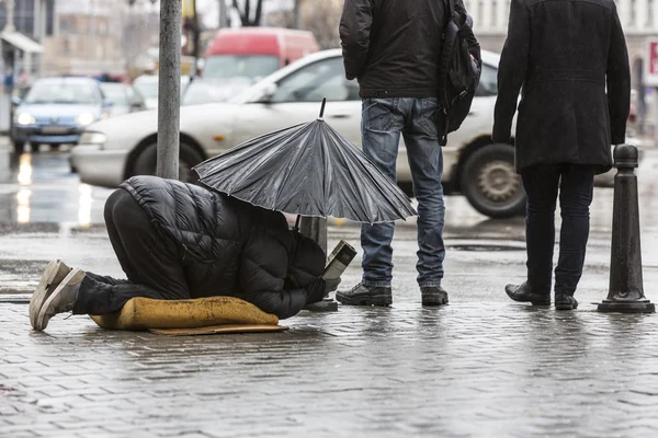 Beggar in the rain with umbrella legs — Stock Photo, Image