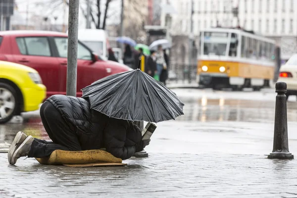 Mendigo na chuva com guarda-chuva tráfego — Fotografia de Stock