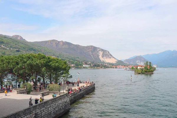 Sarayın pencerelerinden Isola Bella rıhtımının gölgeli ağaç taçlarına kadar panoramik bir manzara. Uzakta, Isola dei Pescatori 'nin ana hatları, Stresa gezinti güvertesi, kıyı tepeleri ve arka planda Alpler' in sıradağları, İtalya.