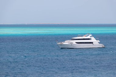 Deniz manzarası, Kızıldeniz 'in masmavi sularının panoramik görüntüsü, arka planda turkuaz mercan resifleri, ufukta beyaz çöl kumu, ön planda beyaz motor yatı.