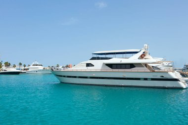 Hurghada Limanı 'ndaki Kızıldeniz' in masmavi sularında beyaz bir motor yatı demirlemiştir. Açık mavi gökyüzü denizin rengini yankılıyor