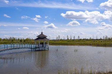 Panoramik manzara, gölün ortasında köprüsü olan Çin çardağı, bulutlu mavi gökyüzünün arka planı, gözlem güvertesi, dinlenme yeri.