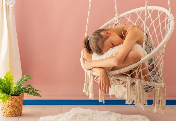 Young girl is relaxing in a hammock chair in a cozy home interior