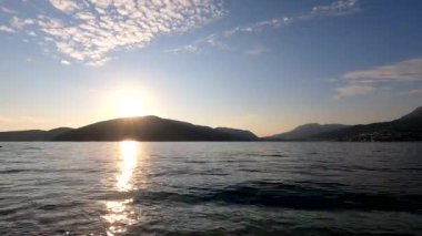 Kotor Körfezi 'nde günbatımının panoraması hızlandırılmış modda. Hareket eden bulutlar, güneş ışınları, sudaki dalgalar, botlar plana dinamik katıyor. Herceg Novi 'nin Forte Rose seti manzarası
