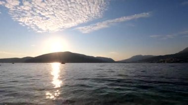 Kotor Körfezi 'nde günbatımının panoraması hızlandırılmış modda. Hareket eden bulutlar, güneş ışınları, sudaki dalgalar, botlar plana dinamik katıyor. Herceg Novi 'nin Forte Rose seti manzarası