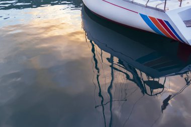 Sakin, sakin deniz manzarası. Yat limanına demirlemiş bir yelkenli zevk teknesinin bir parçası, batan güneşin ışınlarıyla körfezin sakin sularında büyüleyici renklere yansıyor. Karadağ 'ın Kotor Körfezi.