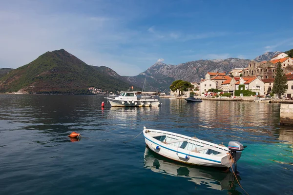 Kotor Körfezi 'nde, dağlarda ve Perast seti üzerinde resim gibi bir deniz manzarası, ön planda bir balıkçı teknesi demirli, silueti suyun sakin yüzeyine yansıyor.