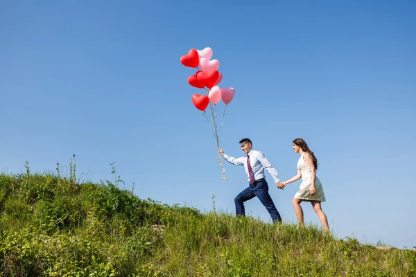 Glückliches Hochzeitspaar mit roten Luftballons — Stockfoto