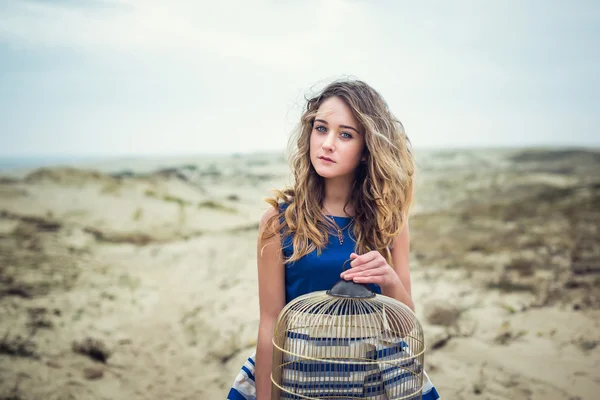 Beautiful girl with a birdcage in a dune — Stock Photo, Image