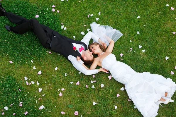 Casal de casamento feliz deitado na grama verde — Fotografia de Stock