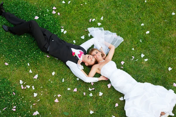 Happy wedding couple lying on green grass — Stock Photo, Image