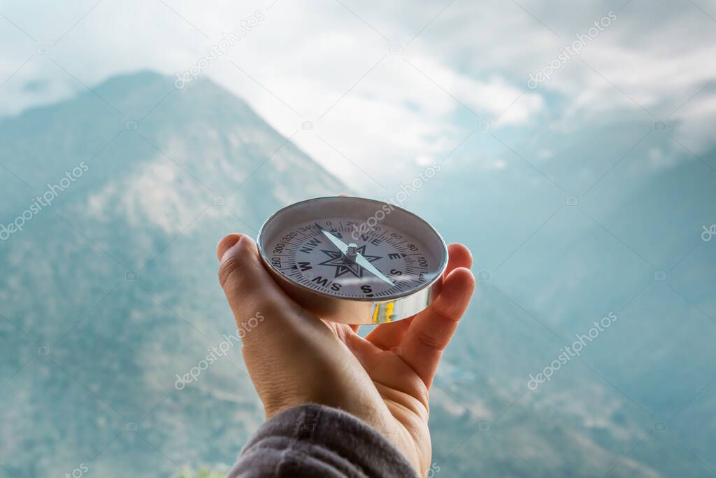 Round compass in hand on the background of blurred mountain. Concept for travelling and active lifestyle.