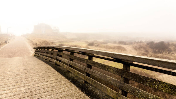 Wooden bridge and road. Autumnal misty morning on the coast of Texel island, the Netherlands.