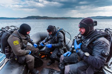 Teriberka, Rusya - 29 Temmuz 2017: Üç dalgıç botta oturmuş, ekipmanlarını kontrol ediyor ve dalmaya hazırlanıyorlar. Barents denizinde çekilmiş..