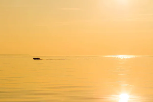 Silhouette of a fishing boat in the sea. Quiet beautiful golden sunset on the sea. Summer nature background
