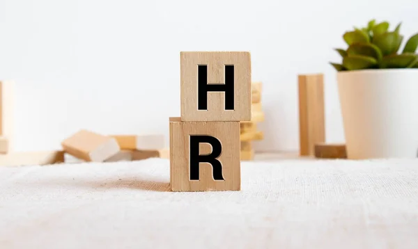 Wooden cube block building the word HR at the center on grid line note book with random other blocks in the background, represent Human Resource department, hiring new job or position in company.