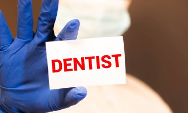 Doktorun mavi eldivenli elleri DENTIST kelimesini gösteriyor. Beyaz arka planda eldivenli bir el. Tıbbi konsept. İlaç.