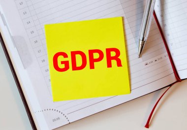 Not defteri, kalem, akıllı telefon ve yeşil bitki, GDPR sözcüğüyle beyaz masanın düz bir görünümü vardı..