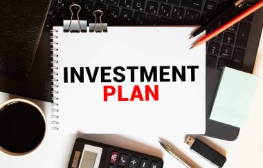Bilgisayarlı INVESTMENT PLAN yazılı ofis masası, akıllı telefon, bir fincan kahve, kalem, hesap makinesi, zar, ataç, dosya ve dosya - iş konsepti üst görünümü.