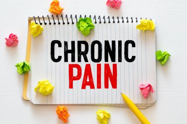 CHRONIC PaIN, steteskop ve siyah çerçeveli gözlüklerin yanındaki ahşap bir masada beyaz bir deftere yazılmıştır. Tıbbi konsept