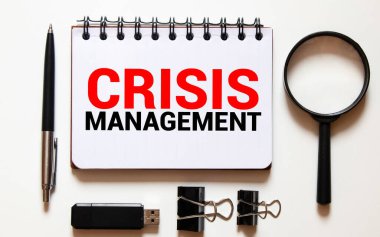 Not defteri yazma CRISIS MANAGEMENT, laptop ve gözlüklü ofis masası.