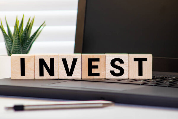 Рука положить монеты штабелирования на деревянный блок, которые печатаются экран инвестировать формулировки с черной стрелкой. Концепция инвестиционного и делового роста