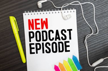Kırsal ahşap masadaki podcast kayıt ekipmanlarının en üst görüntüsü. Spiral not defterinde yeni podcast bölümü yazıyor.