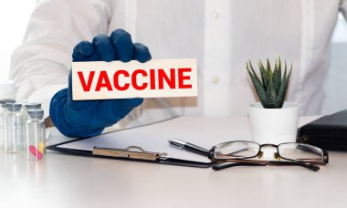 Ellerinde koruyucu eldivenlerle kağıt üzerinde AVCCINE kelimesi. Arka planda bulanık kadın doktor.