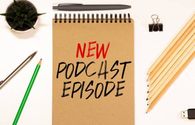 Not defterinde mikrofon, bilgisayar klavyesi ve kulaklıkla birlikte NEW PODCAST EPISODE 'nin üst görünümü, podcast kavramı